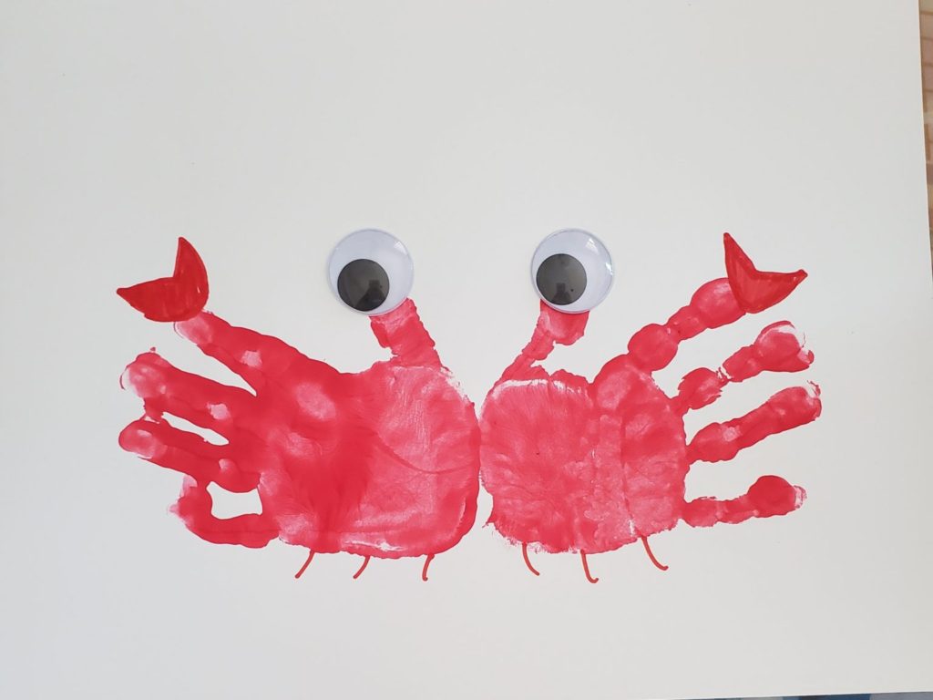 Preschool Ocean theme craft of two red toddler hand prints on a piece of paper with palms touching in middle to look like a crab