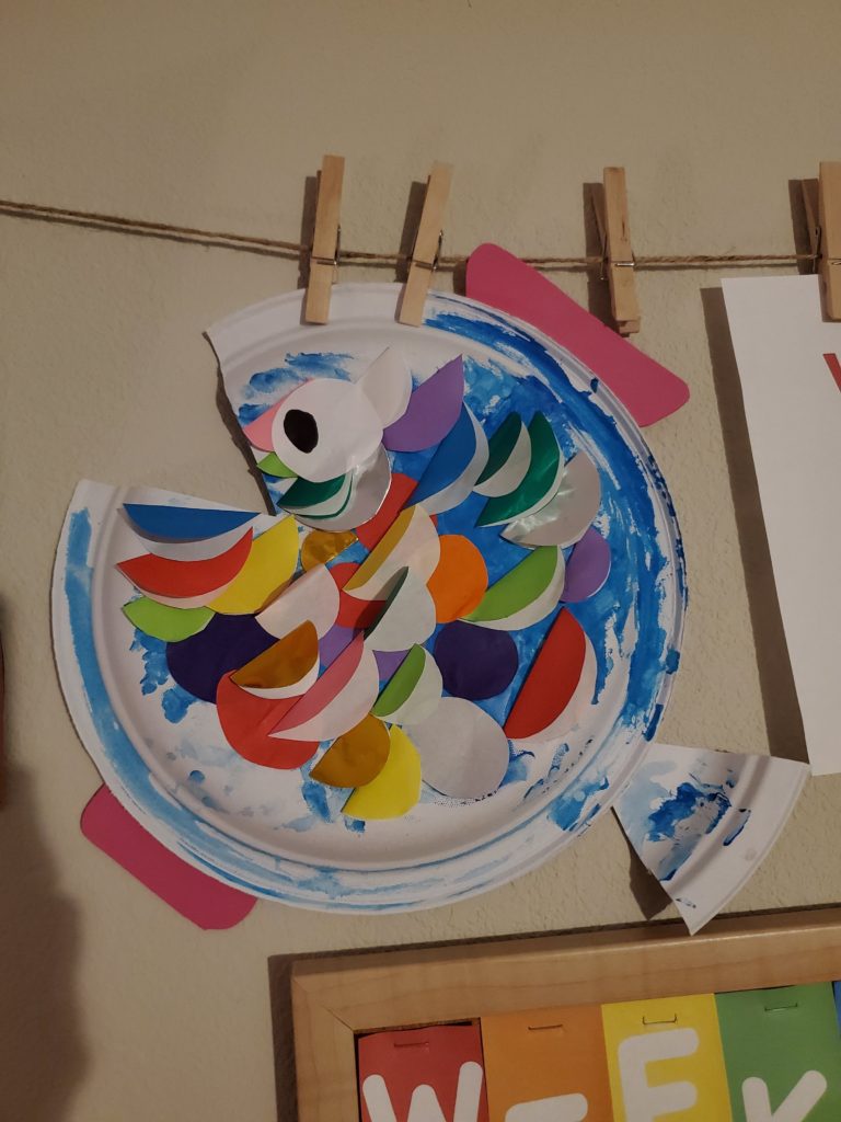 kid craft of a paper plate with triangle mouth cut out and paper fins and multiple colored gills to resemble a fish