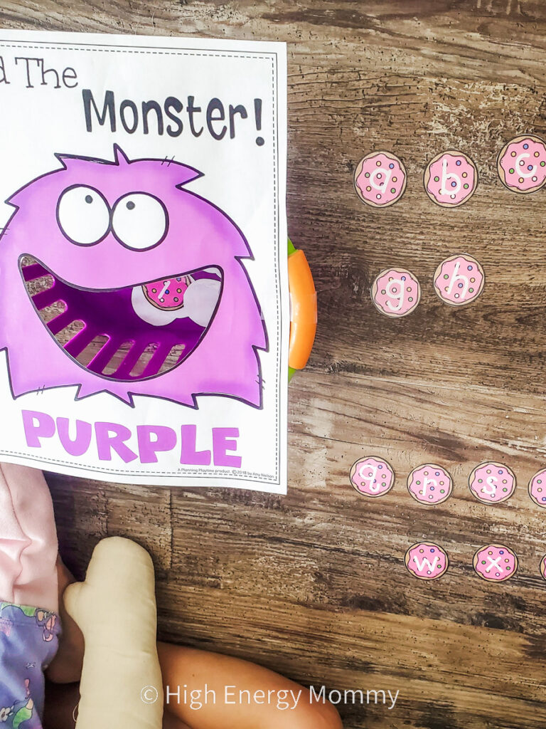 Printed picture of a purple cartoon monster face with it's mouth cut out and paper alphabet cookie letters next to the monster's face to feed it.