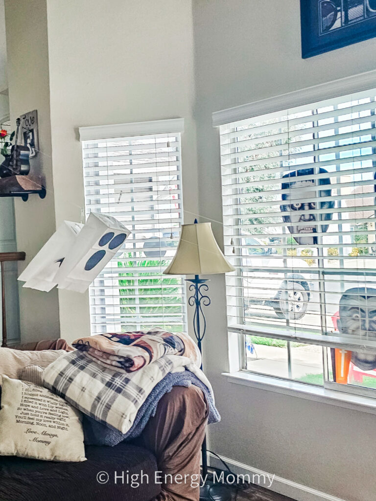 living room with 2 white paper bag ghosts going down a zipline made of fishing line in front of large window