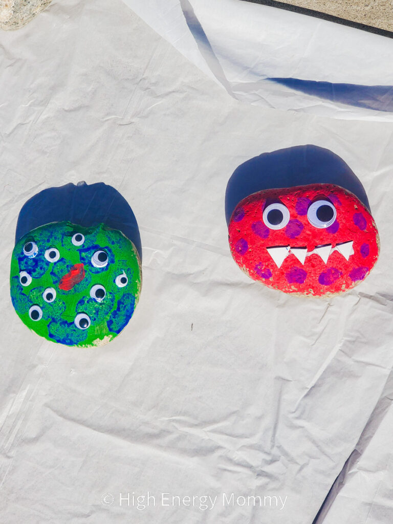 painted green rock with blue spots and googly eyes all over it and a painted red rock with purple spots, triangle teeth and googly eyes