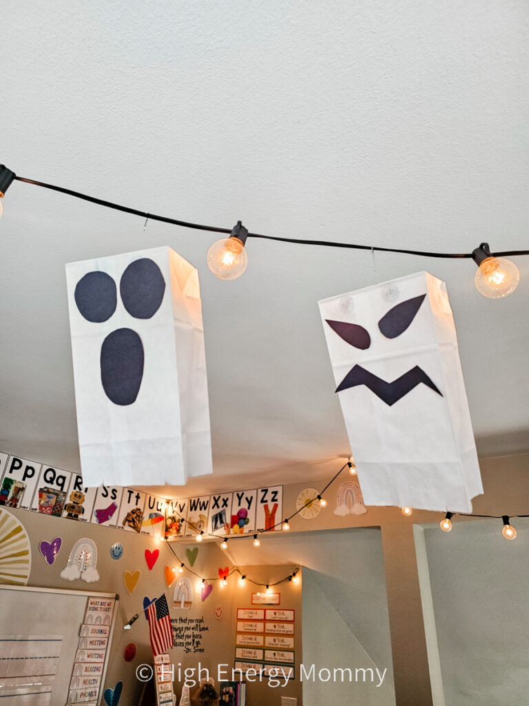 white paper lunch bags with faces like ghosts, hanging from a strand of lights