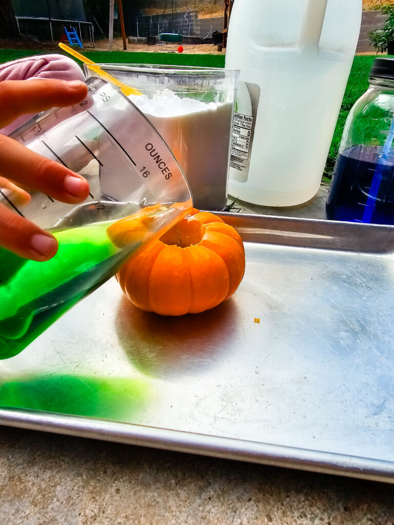 Mini pumpkin with hole in top and green liquid being poured in for science experiment