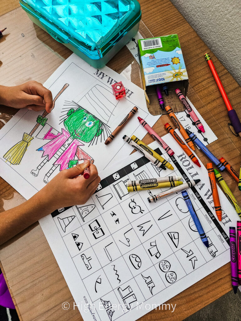 overhead view of a child's school desk with crayons all over and a picture of a with drawn as part of a drawing game 