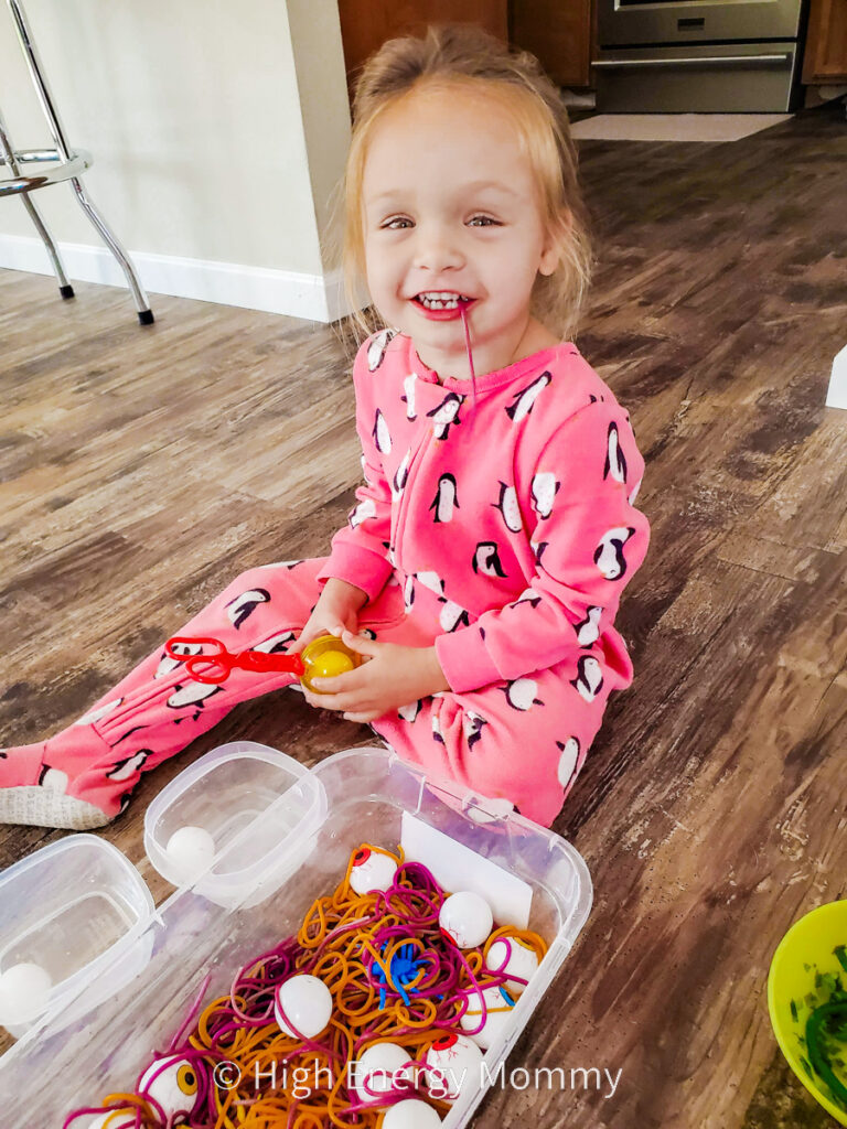 Toddler girl with cooked purple spaghetti noodle hanging out of her mouth