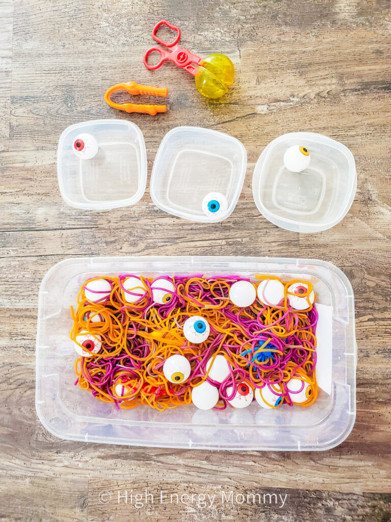 colored spaghetti noodles in a container with plastic eyes and plastic spiders