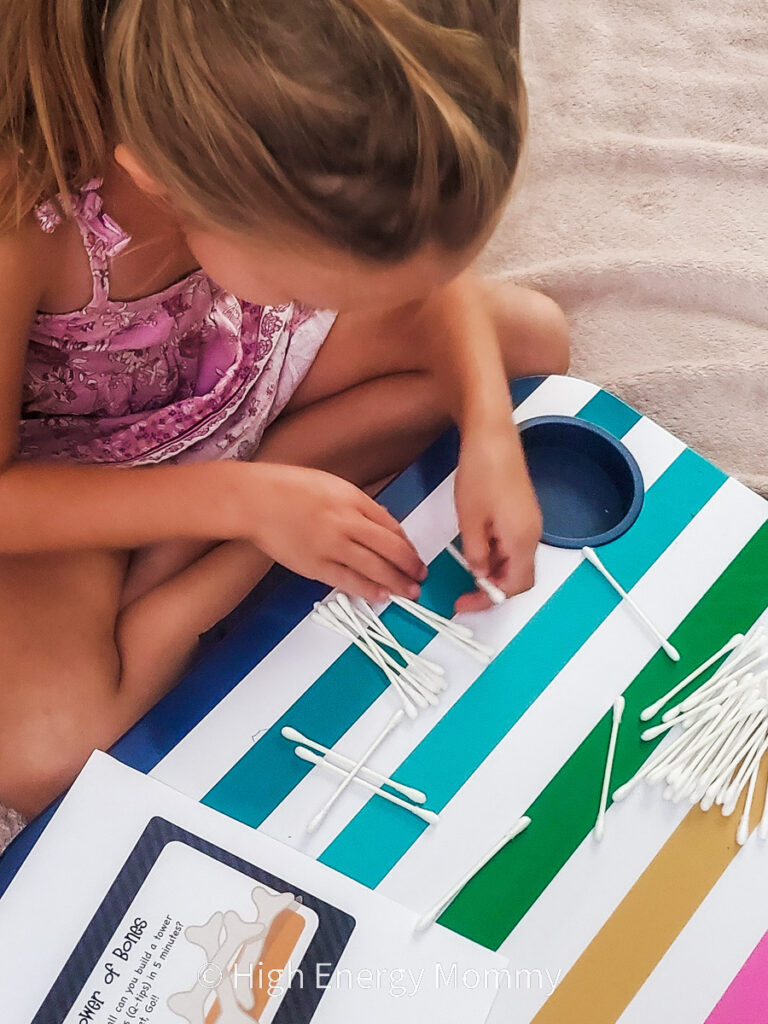 Kindergarten age girl stacking cotton swabs as "skeleton bones" on a colorful striped tray