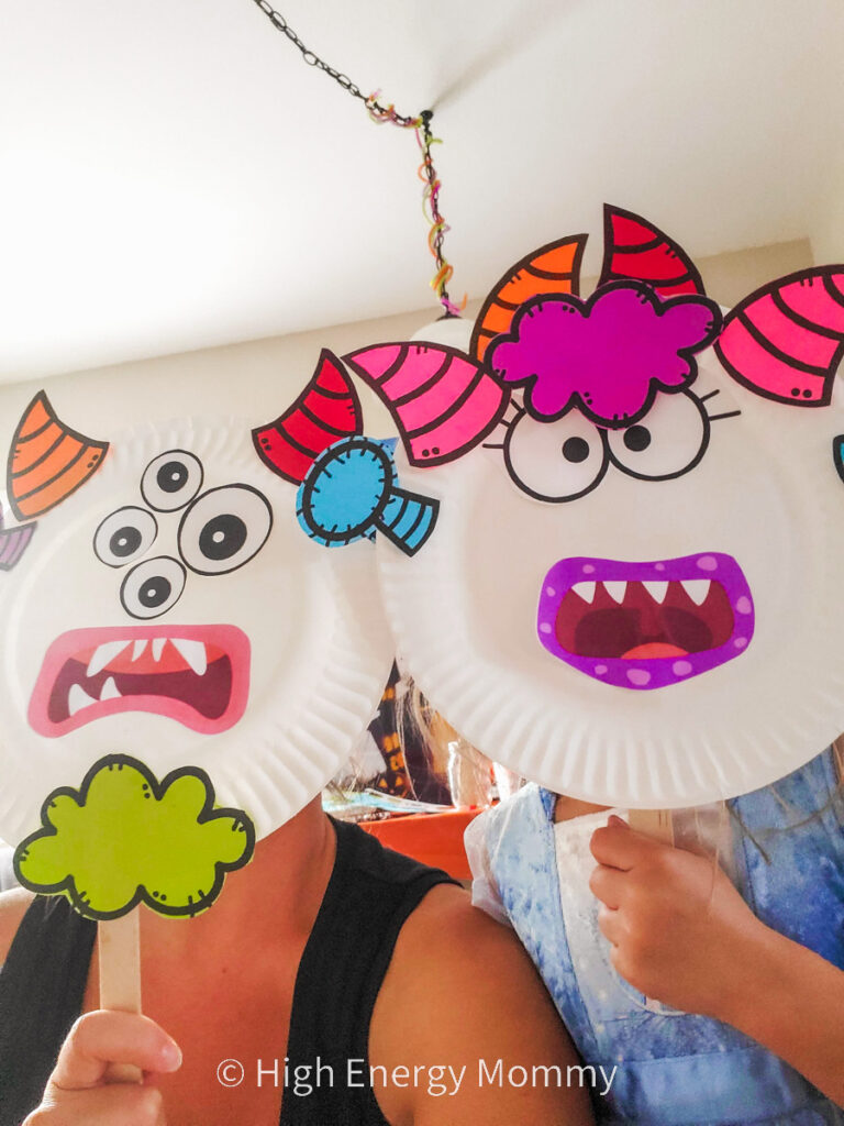 two people holding up whit paper plates with monster face pieces glued to the plates like for a photo prop