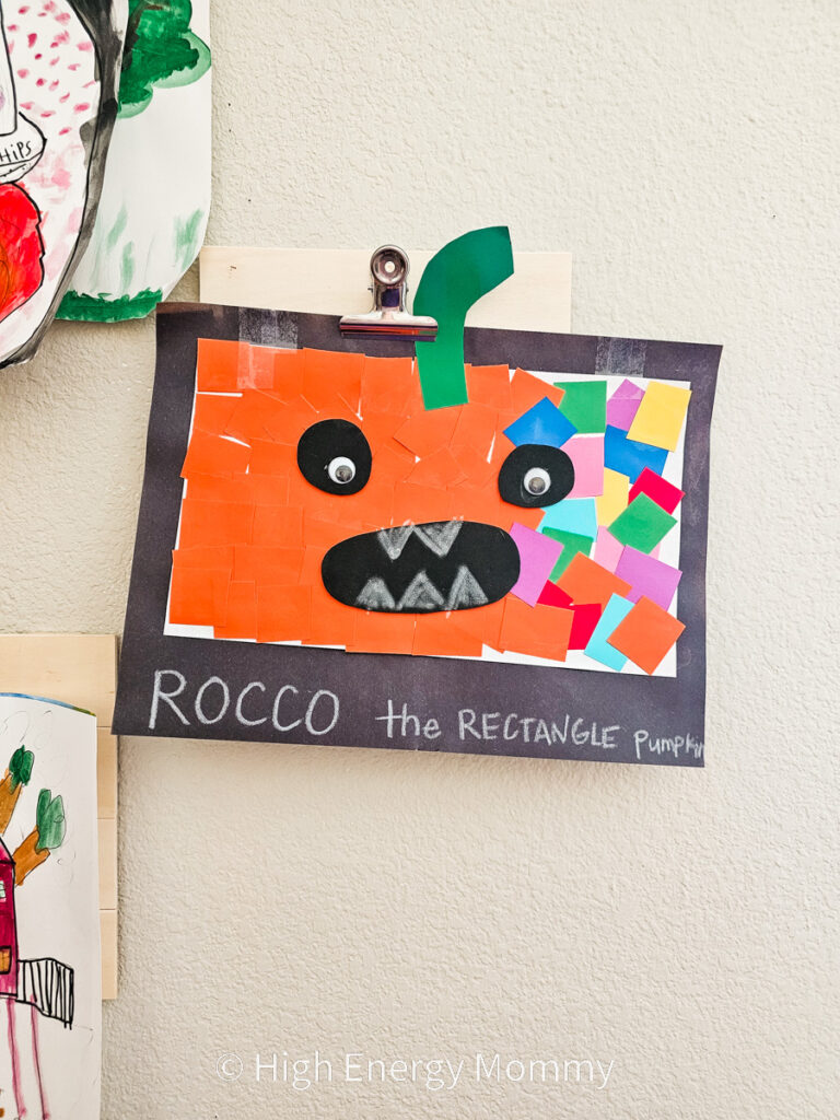 Black rectangle piece of construction paper with an orange rectangle with the right side having multiple colored squares on the pumpkin and a face and stem