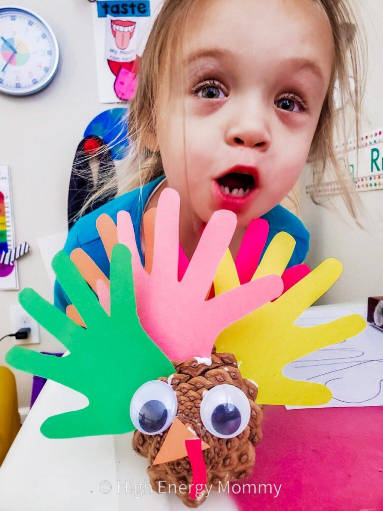 Cute turkey crafts for kids pinecone that looks like a turkey with googly eyes and construction paper beak with colorful construction paper feathers made from child's traced handprints