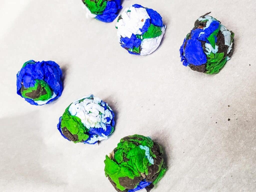 homemade seed bombs made with blue, white, brown, and green paper laid out in 2 rows