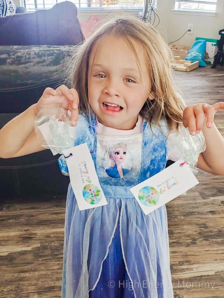 Little girl in blue dress holding up a small gift in a decorative plastic bag each hand