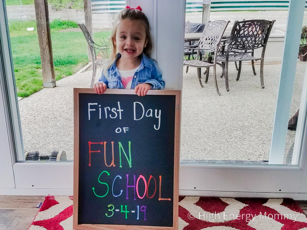 toddler girl holding a chalkboard sign that says First Day of Fun School