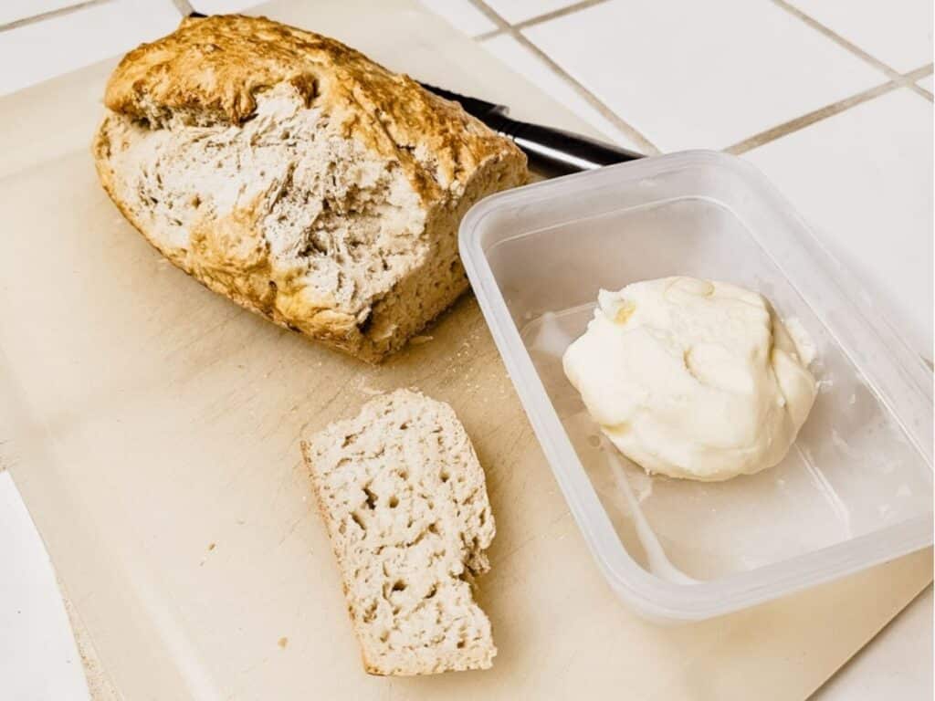Loaf of homemade bread next to a small container of butter, ready to slice and serve.