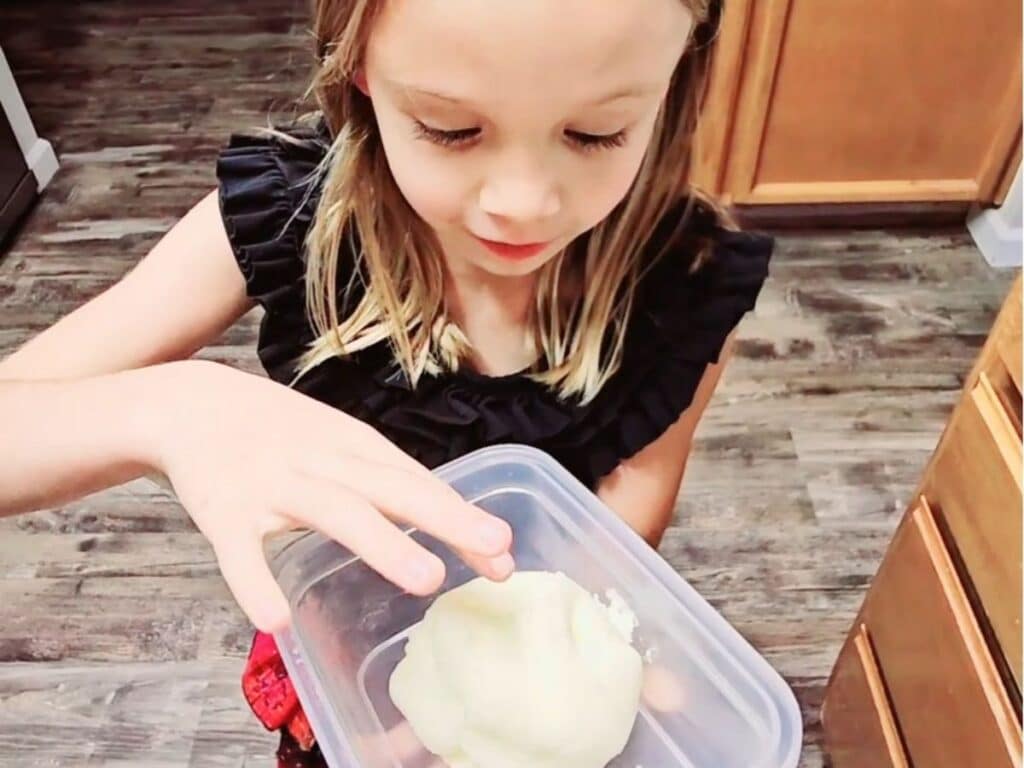 Child holding a container of freshly made solid butter with an amazed expression on her face.