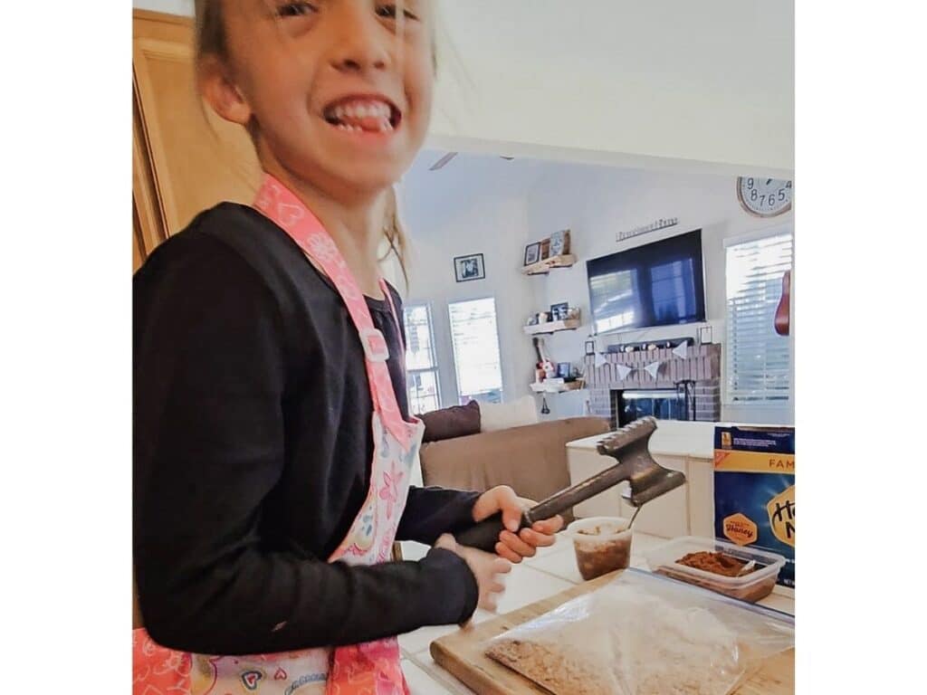 Child smashing graham crackers in a zip-top bag to make the crust for mini mason jar desserts.
