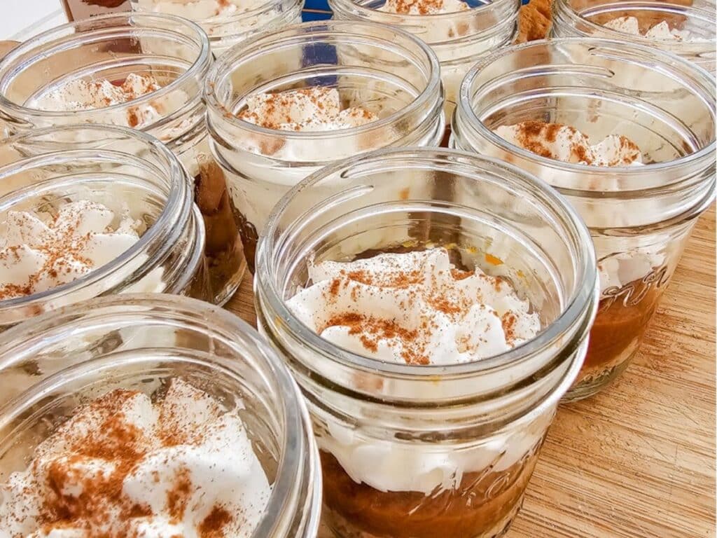 Close up image of mini mason jar desserts topped with whipped cream and cinnamon, shown without lids